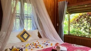 A bed with a canopy, a bedside table with a teapot, and a window with curtains. - PHU QUOC POMELO GARDEN (Phu Quoc)