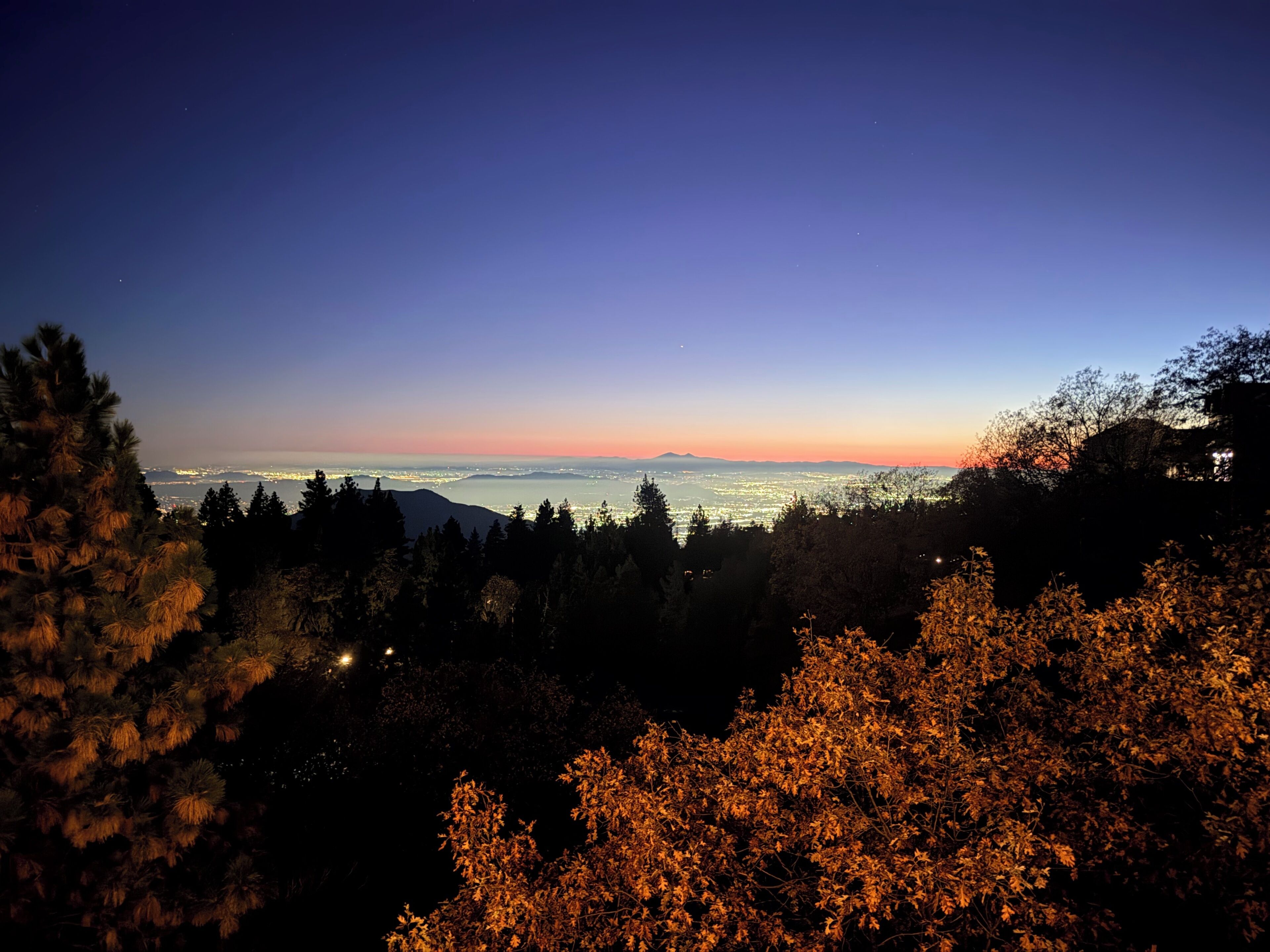 Ein Nachtblick auf eine Stadtlandschaft mit fernen Bergen und wolkenlosem Himmel.