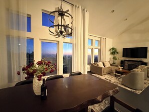 Ein modernes Wohnzimmer mit Esstisch, Sofas, Fernseher und großen Fenstern.