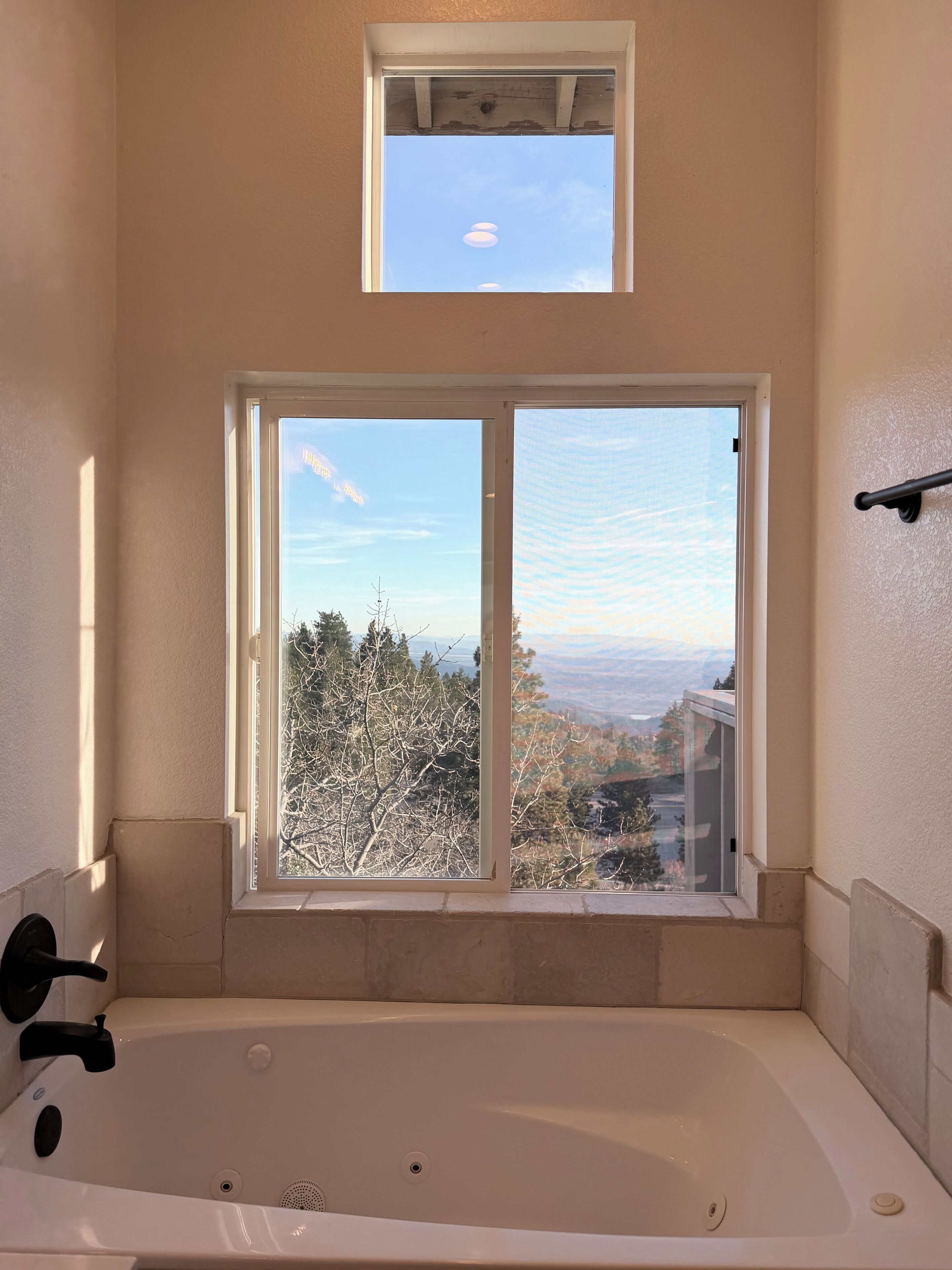A bathroom with a bathtub, a window with a view of trees and hills, and a small skylight above the window.