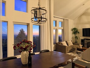 Ein modernes Wohnzimmer mit Esstisch, Stühlen, einer Couch, einem Fernseher und großen Fenstern mit Blick.