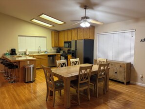 Eine moderne Küche mit Holzausbau, einem Essbereich mit Tisch und Stühlen, einer Edelstahlmülltonne und einem Deckenventilator.