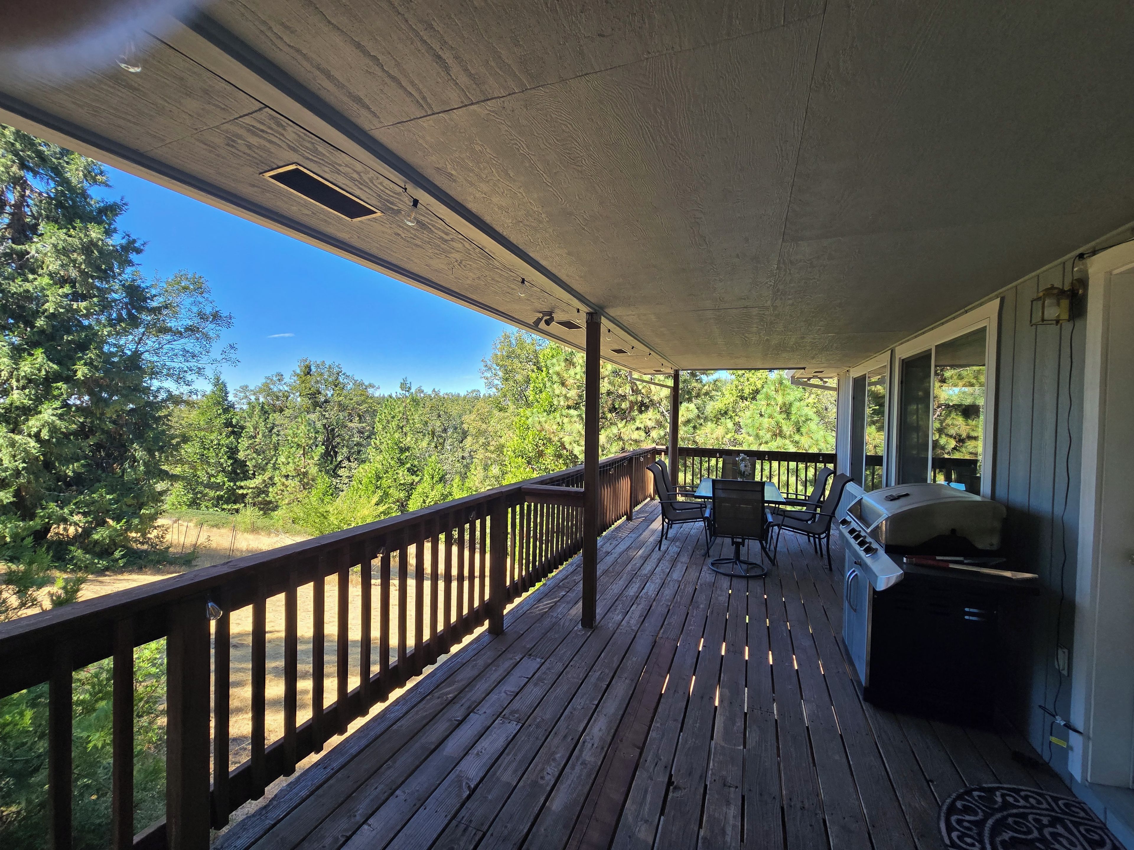 A covered porch with a wooden deck, a barbecue grill, and a table with chairs.
