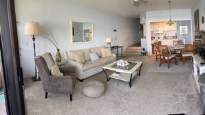 A living room with a sofa, coffee table, and dining area with chairs. There is a kitchen in the background. - OCEANFRONT with Private Beach! Hale Mahina A206 (Lahaina)