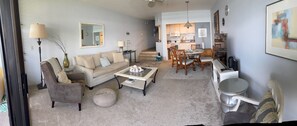A living room with a sofa, coffee table, and dining area with chairs. There is a kitchen in the background. - OCEANFRONT with Private Beach! Hale Mahina A206 (Lahaina)