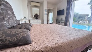 A bedroom with a large bed, a dresser, a mirror, a lamp, and a TV. There is a window with a view of a pool. - Typically Provençal, located in the hills above Les Issambres, 6+1 (LES ISSAMBRES)
