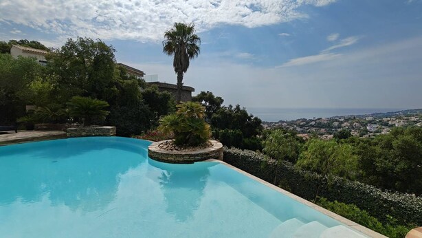 A swimming pool with a stone edge, surrounded by greenery and a view of a coastal town. - Typically Provençal, located in the hills above Les Issambres, 6+1 (LES ISSAMBRES)