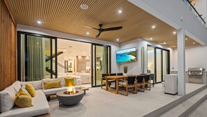 Ein modernes Wohnzimmer mit Sofa, Couchtisch und Essbereich, verbunden mit einer Küche mit Fernseher und Grill.