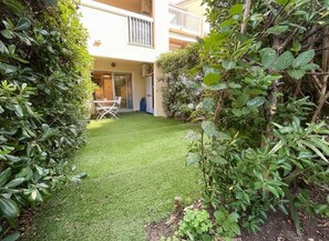 A well-maintained garden with a lawn, surrounded by dense foliage and a building in the background. - Studio de Charme avec Jardinet Privatif – Cœur du Golfe de Saint-Tropez (COGOLIN)