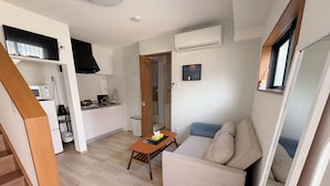 Un espai vital compacte amb un sofà, una taula petita, una zona de cuina i una escala.