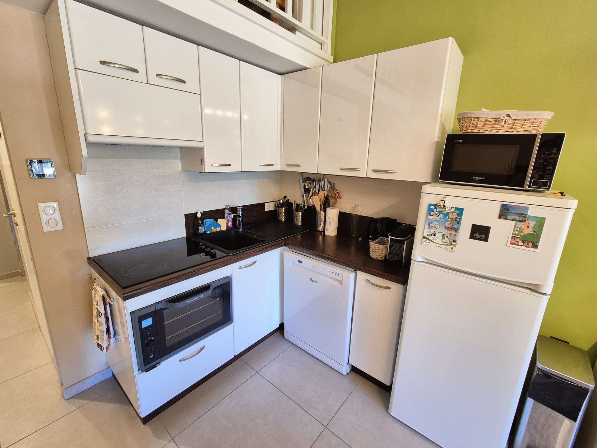 A compact kitchen with white cabinets, a black countertop, a built-in oven, a microwave, and a refrigerator.