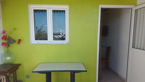 A room with a bright green wall, a white-framed window, a small table, and a door leading to another room. - Charming room in St Philippe, between the sea and the mountains, close to the GRR2 footpaths. (Saint-Philippe)