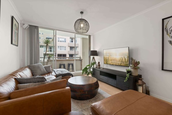 Ein modernes Wohnzimmer mit einer Ledersofa, einem runden Couchtisch und einem Flachbildfernseher auf einer dunklen Ablage.