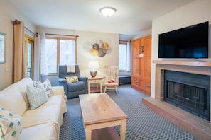 Ein Wohnzimmer mit Sofa, Sessel, Couchtisch, Kamin, Fernseher und Wanddekoration.