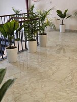 Um corredor com piso de mármore, plantas em vasos e corrimão de metal.