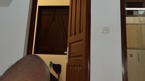 Een kamer met een aan de muur bevestigde televisie, een houten deur en een betegelde vloer.