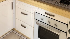 Een keuken met een magnetron, fornuis en oven. Daarboven bevindt zich een kast en er is een betegelde achterwand.