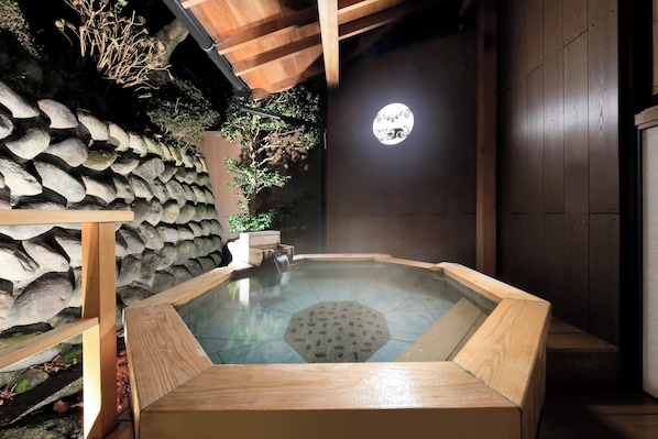 A traditional Japanese onsen with a stone wall, wooden benches, and a wooden ceiling.