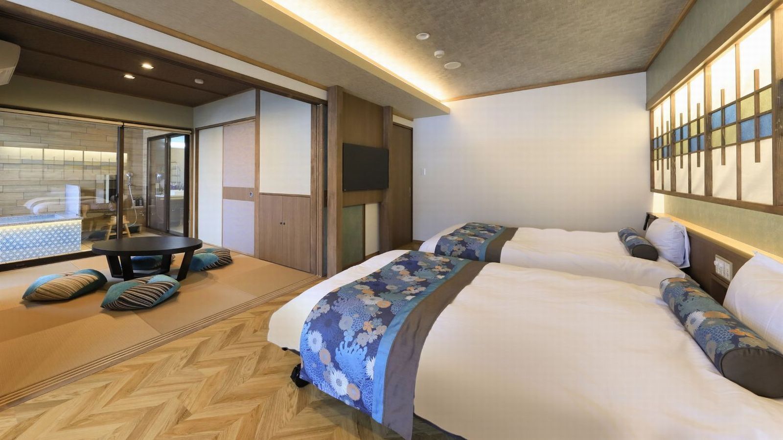 A hotel room with a bed, a desk, and a seating area with cushions.