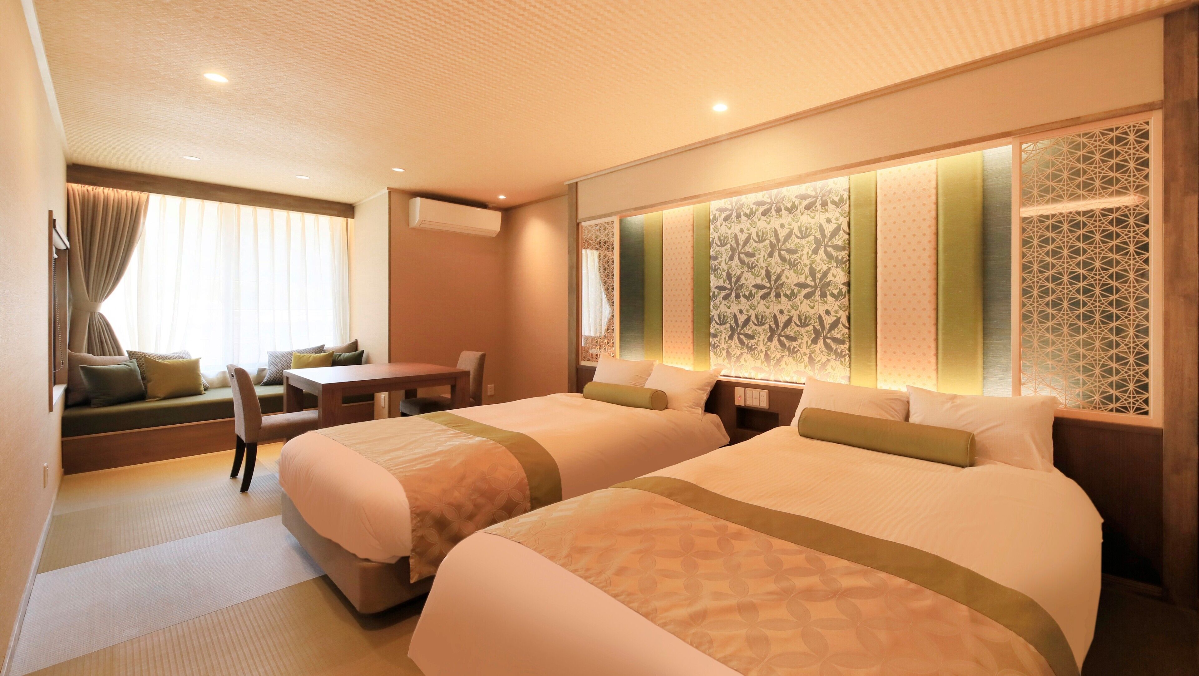 A hotel room with two beds, a sofa, a table, and a view of the outside.