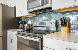 Una cocina moderna con electrodomésticos de acero inoxidable, armarios blancos y un salpicadero de azulejos.
