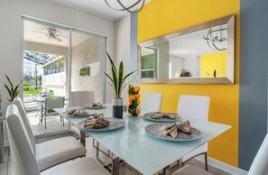 Un comedor moderno con una mesa de vidrio, sillas blancas y una pared de acento amarilla.