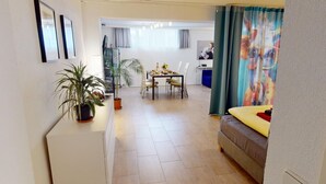 A living room with a sofa, a dining table with chairs, a TV, and a potted plant. - Apartment Konstanz - Urban living for fitters, business travelers and holidaymakers (Konstant)