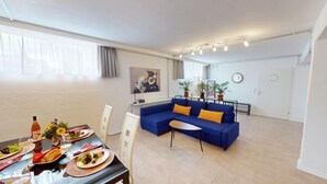 A modern living room with a blue sofa, a dining table set with plates and glasses, and a small side table. - Apartment Konstanz - Urban living for fitters, business travelers and holidaymakers (Konstant)
