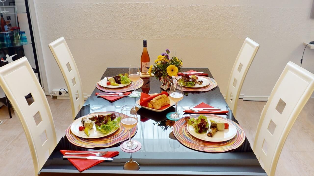 A dining table set for four with plates, glasses, and a bottle of wine.