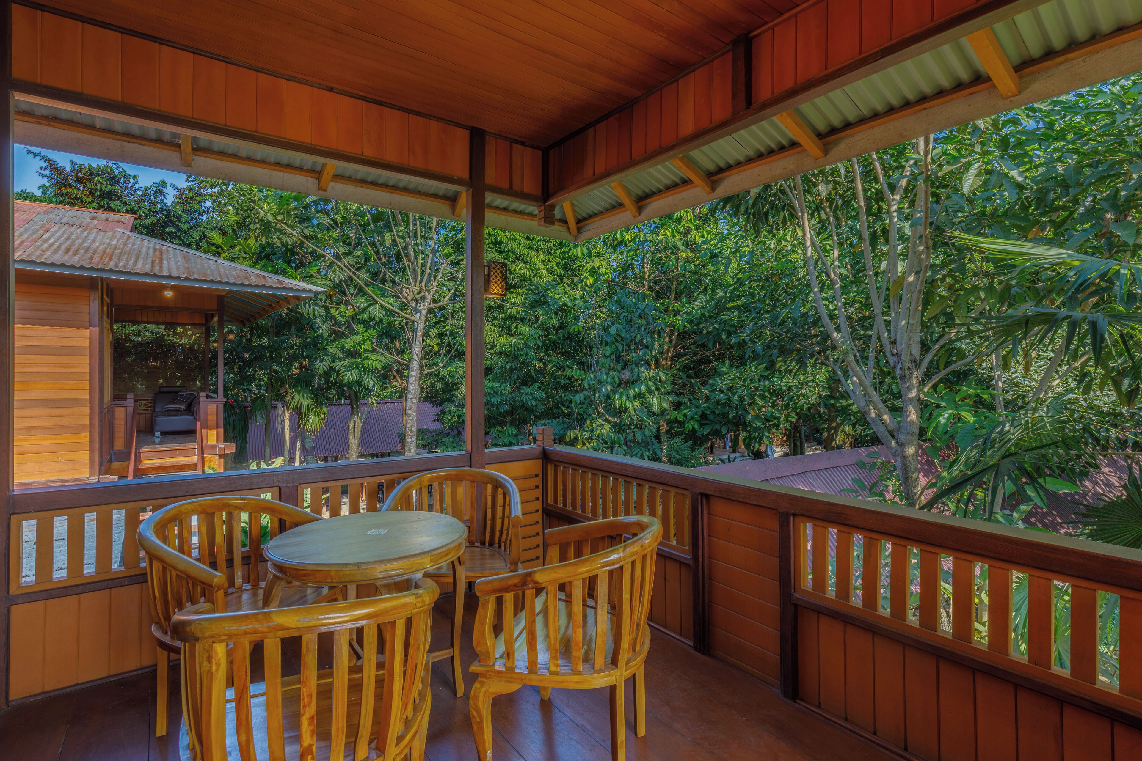 Una terraza de madera con una mesa y sillas, rodeada de abundante vegetación y árboles.