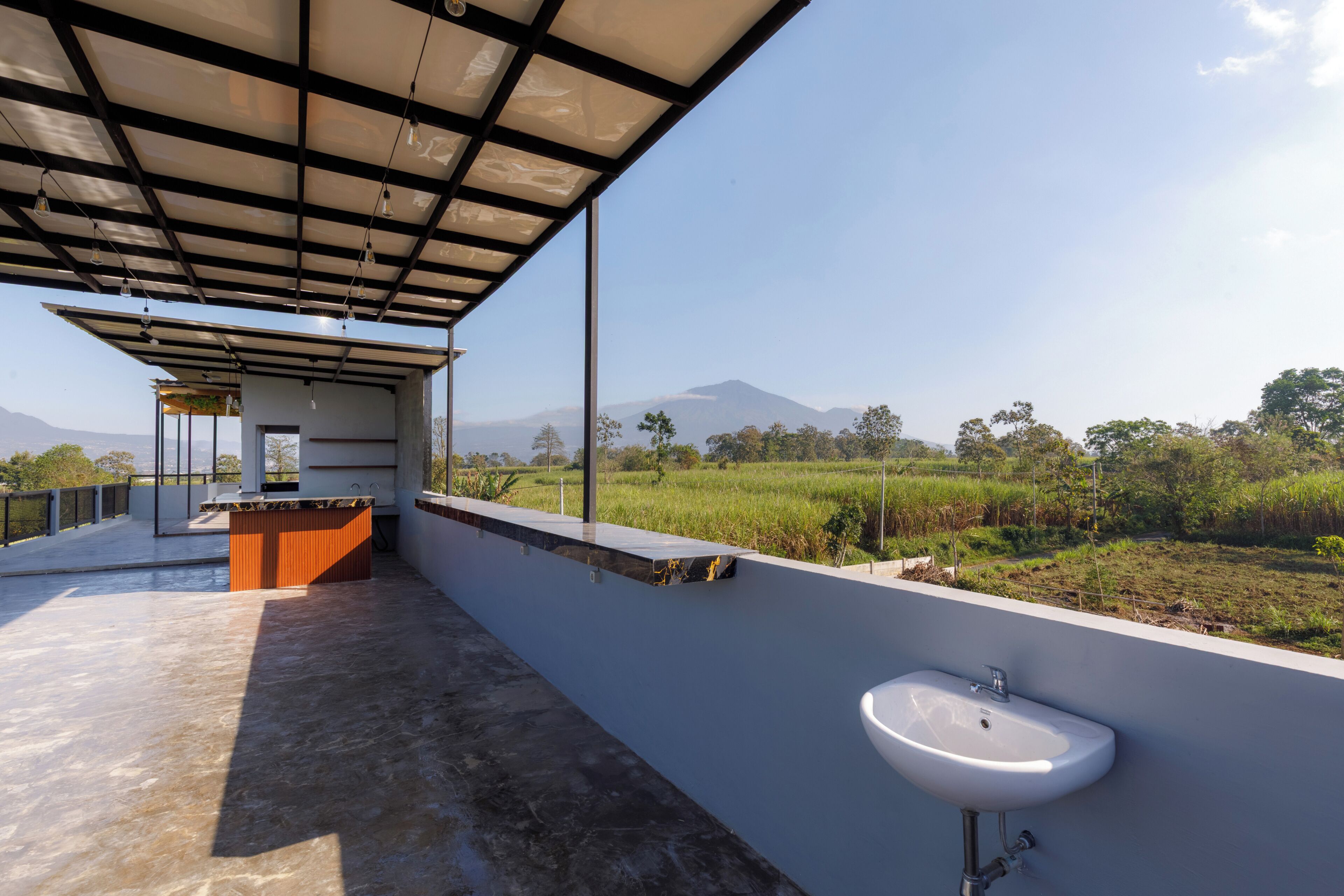 A covered outdoor area with a sink and a view of a green landscape.