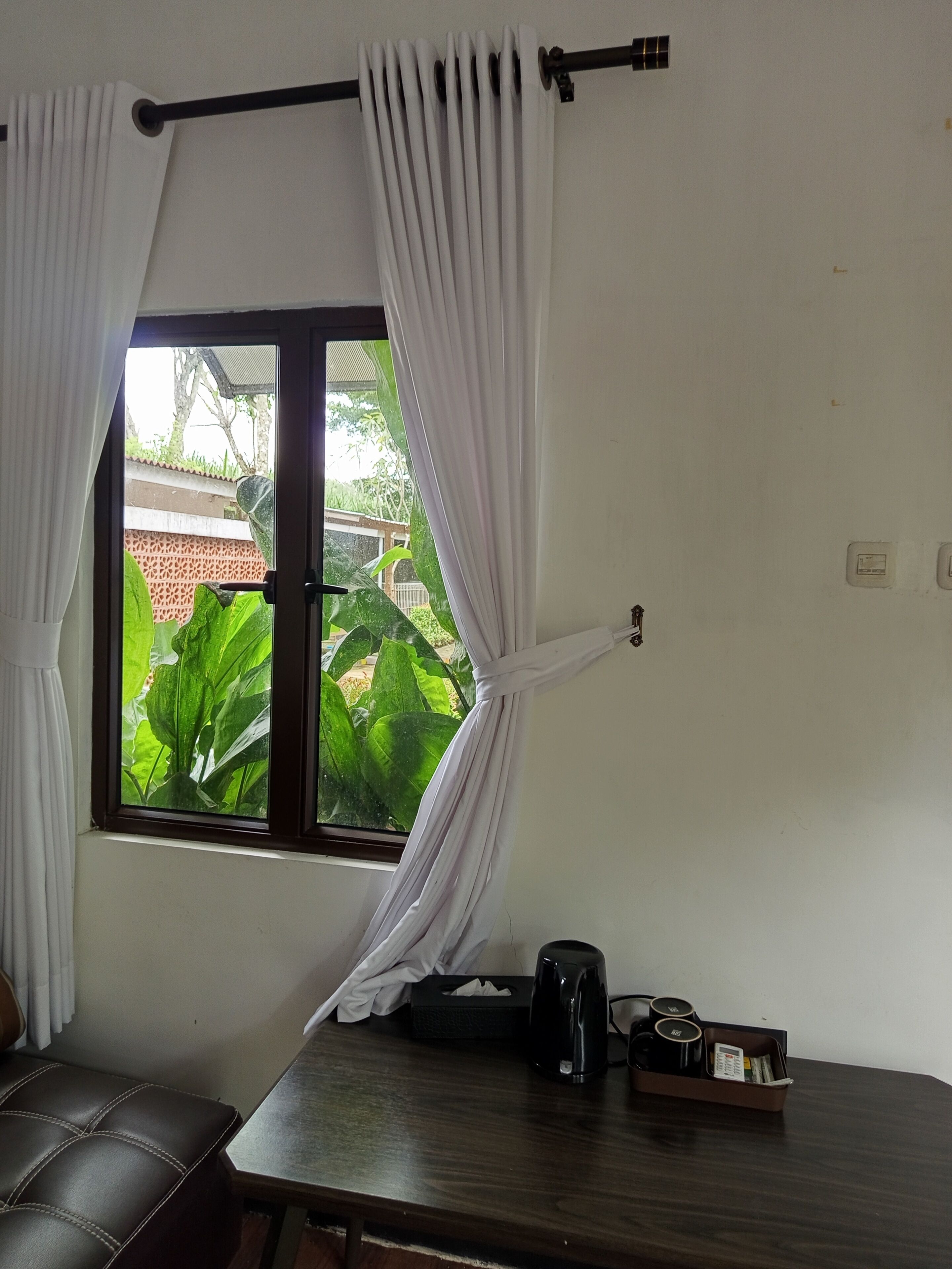 A room with a window, a table with a tissue box, a kettle, and a tray with cups and a menu.
