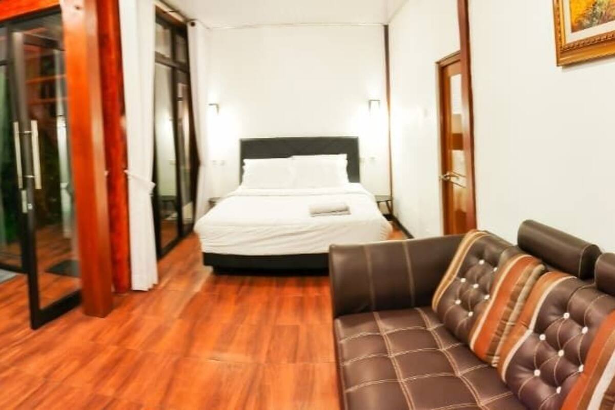 A hotel room with a sofa, a bed, and a sliding glass door leading to a balcony.
