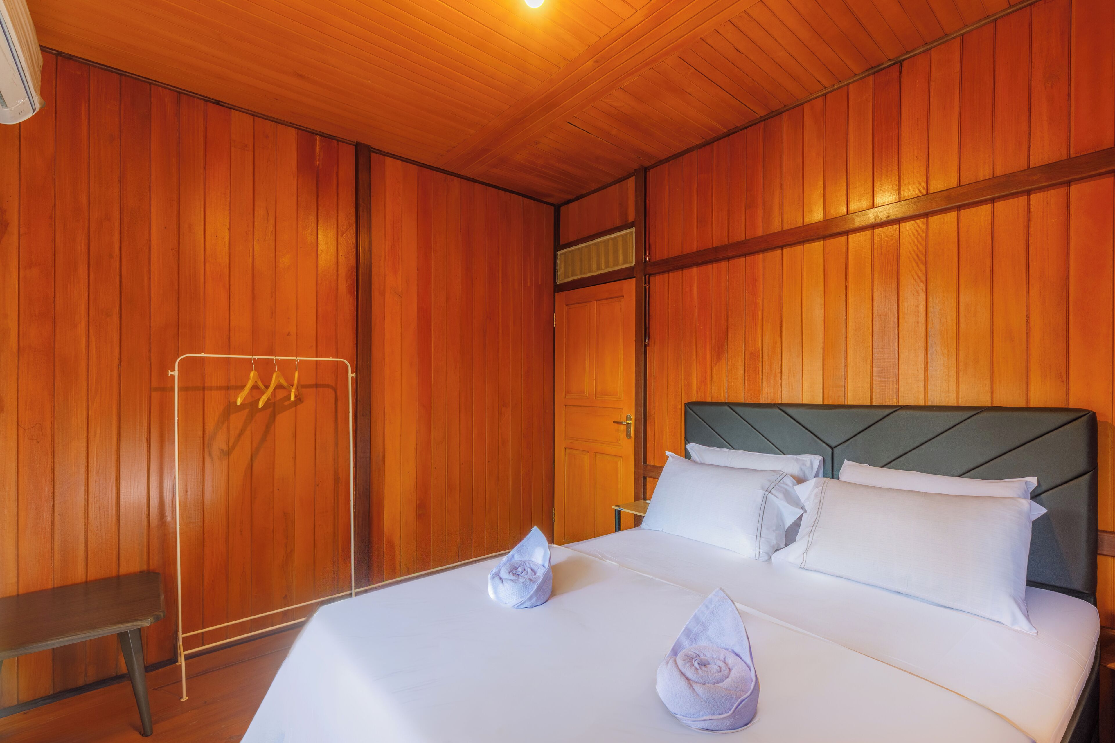 Una habitación de hotel con paredes de paneles de madera, una cama con ropa blanca y un banco.