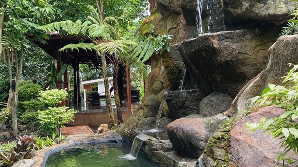 A tranquil garden with a pond, a waterfall, and a gazebo. - Ratu Roso Resort (Ulesari)