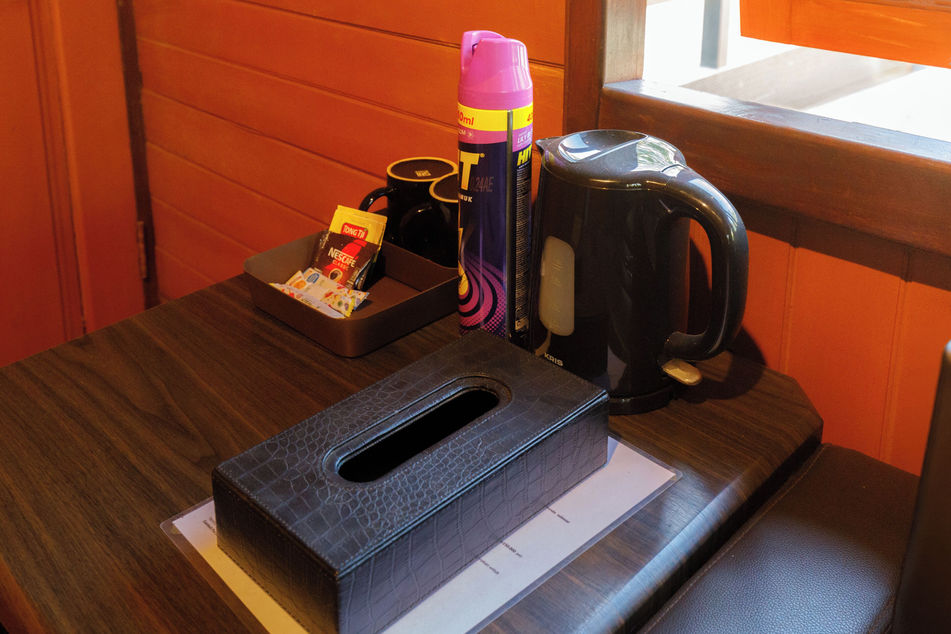 A wooden table with a black leather case, a pink and yellow thermos, a black mug, and a Nescafe coffee packet.