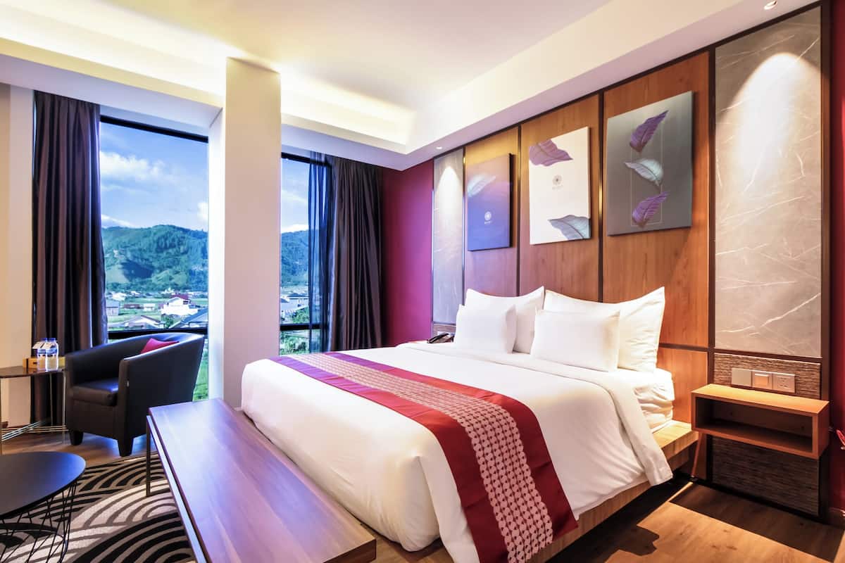 Ett hotellrum med en stor säng, ett skrivbord, en stol och utsikt över ett bergigt landskap genom fönstret.
