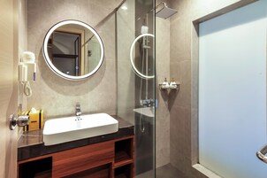 Un baño moderno con lavamanos blanco, un espejo redondo, cabina de ducha con mampara de vidrio y tocador de madera.