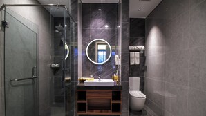 A modern bathroom with a glass shower enclosure, a round mirror, a white sink, and a toilet. - Gayo Petro Hotel (Takengon)