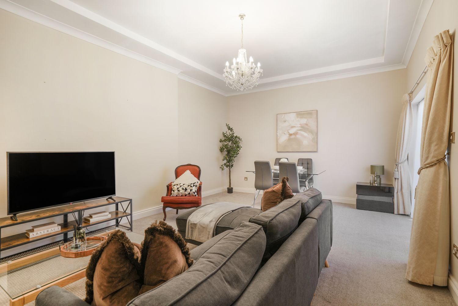 A living room with a television, sofa, armchair, dining table, chairs, chandelier, and a potted plant.
