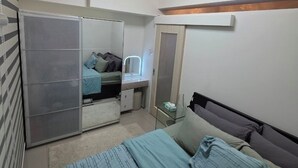 A bedroom with a bed, a wardrobe, a vanity with a mirror, and a ceiling light. - Cozy 1-bedroom riverfront condo in serene area with AC (Mandaluyong City)