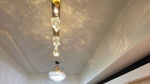 A modern living room with a grey sofa, a flat-screen TV, a chandelier, and a small rug. - Cozy 1-bedroom riverfront condo in serene area with AC (Mandaluyong City)