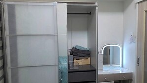 A compact bedroom with a sliding closet door, a vanity with a mirror and lights, and a small bedside table. - Cozy 1-bedroom riverfront condo in serene area with AC (Mandaluyong City)