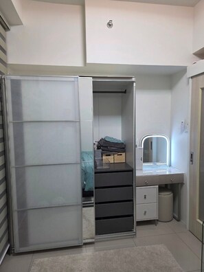 A compact bedroom with a sliding closet door, a vanity with a mirror and lights, and a small bedside table. - Cozy 1-bedroom riverfront condo in serene area with AC (Mandaluyong City)