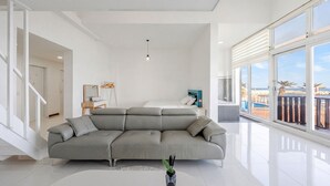 Una sala moderna con un sofá seccional gris, una mesita con un jarrón y un ventanal con vistas a la playa.