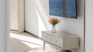 Un mueble blanco con un jarrón de flores rojas, un espejo y una puerta que da a otra habitación.