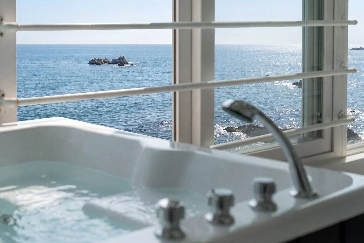 A bathtub with a view of the sea through a window.