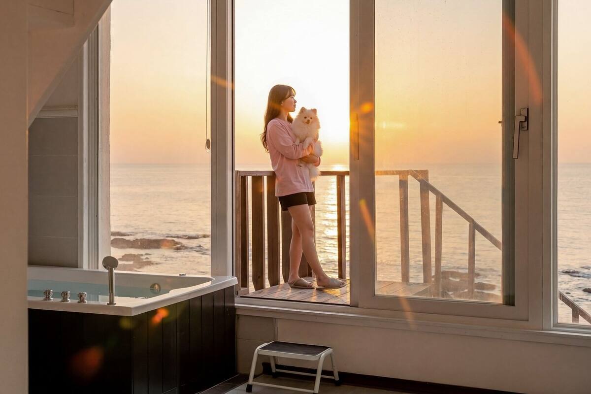 A room with a large window overlooking the ocean, a bathtub, and a small step stool.