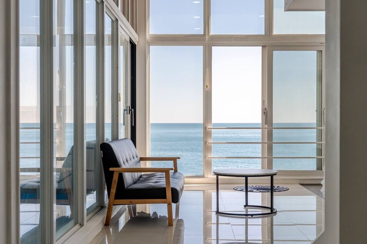 A room with a view of the sea, a chair, and a small table.