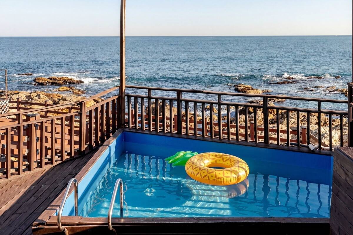A pool with a view of the ocean, surrounded by wooden deck and railings.